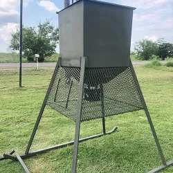 A green, custom metal fabricated deer feeder sitting in a field